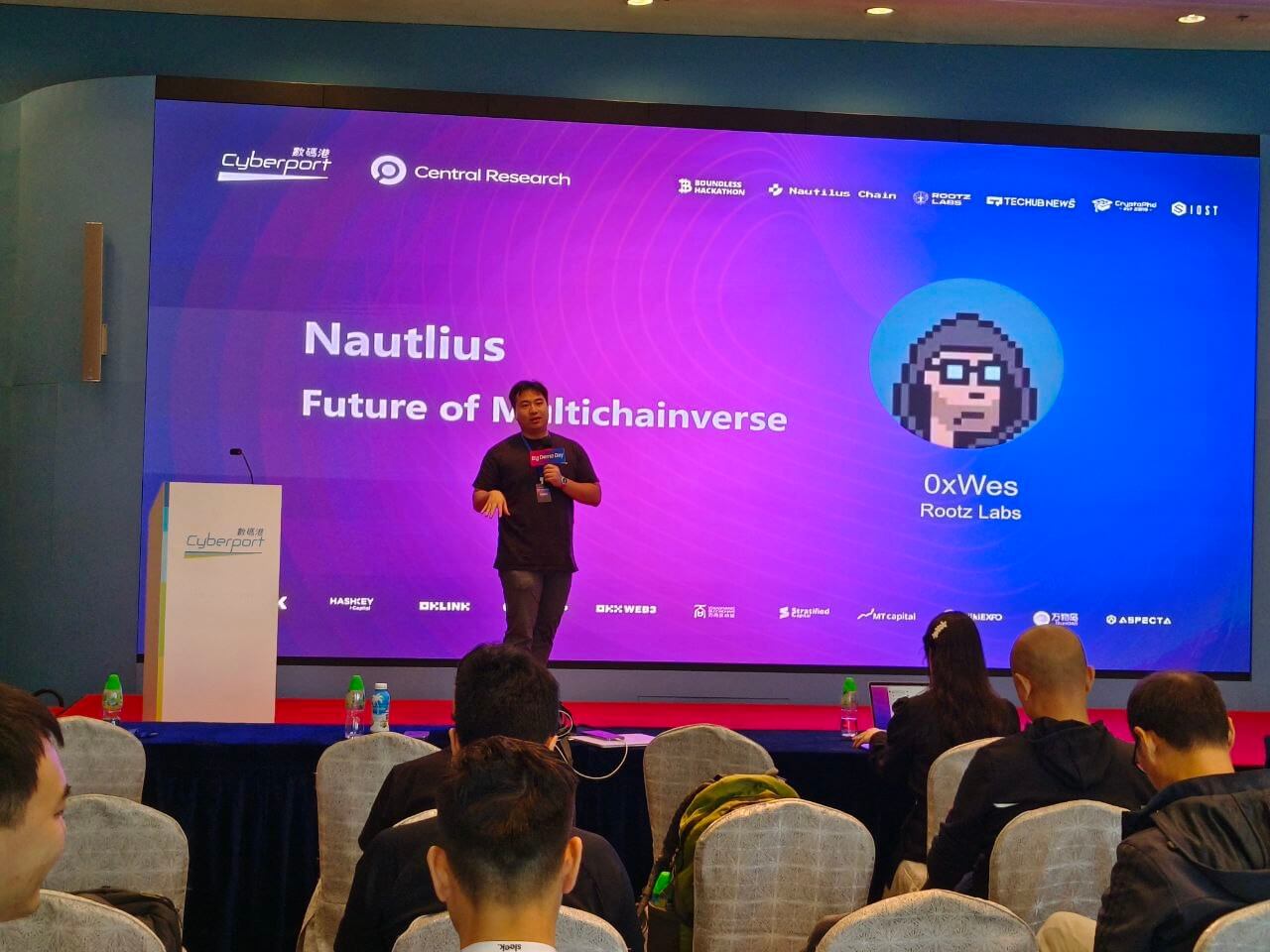 Speaker presenting Nautilus Future of Multichainverse with pixel avatar 0xWes at Cyberport event.